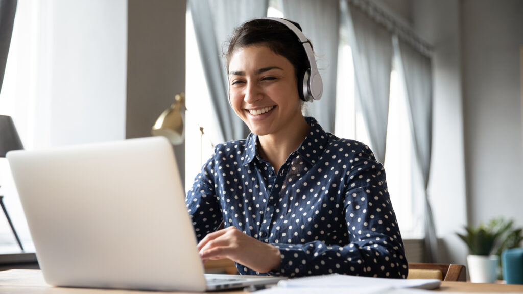smiling woman and cybersecurity professional in blue shirt at computer with headphones