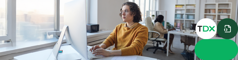 Person at desk with computer in bright office, colleague in background