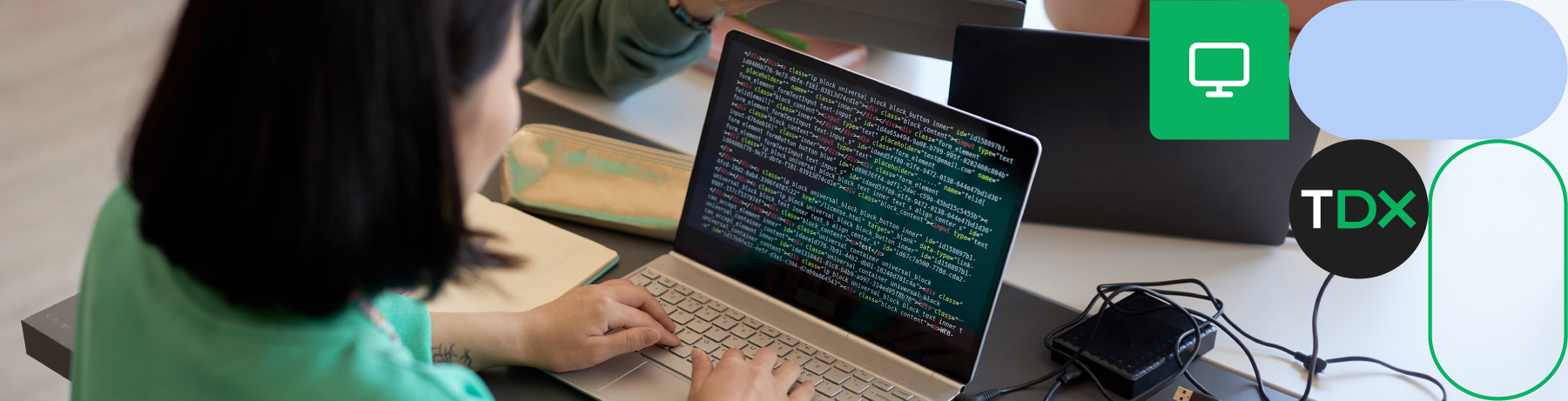 Person coding on a laptop with screen showing programming code, TDX icon on right. 